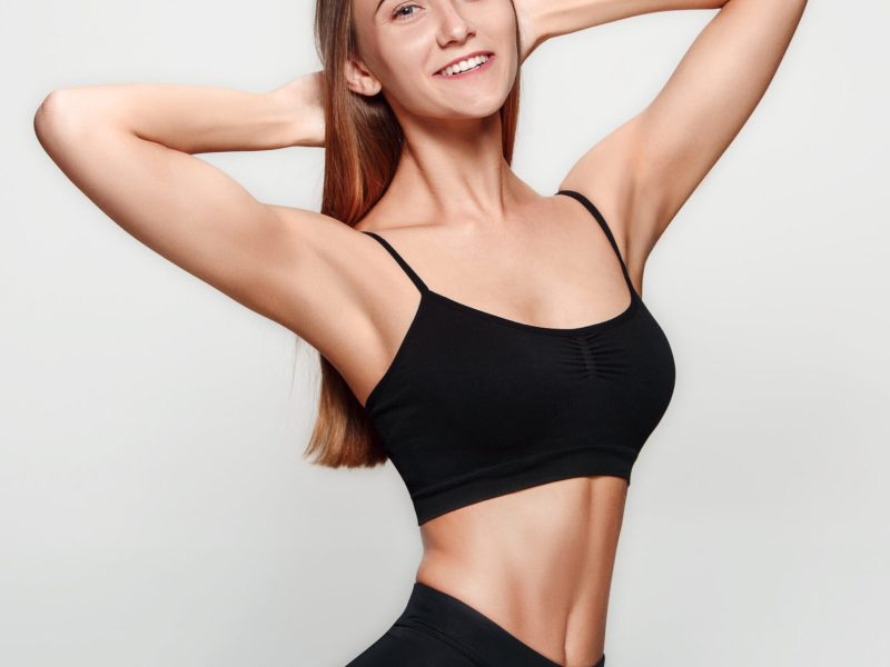 Muscular young woman athlete posing on gray studio background